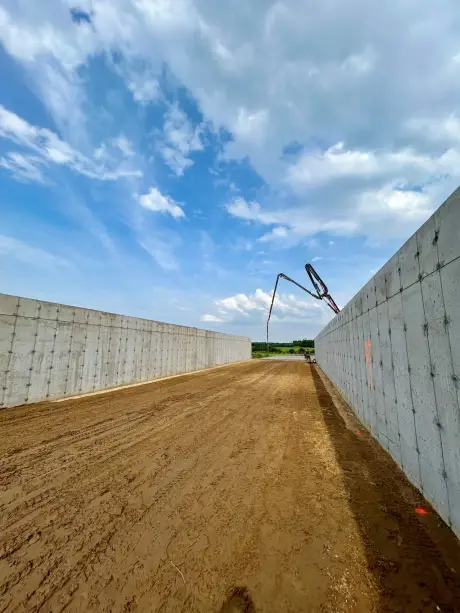 Deux longs murs de fondation coulés en parallèle, la flèche d’une pompe à béton au fond du chantier.