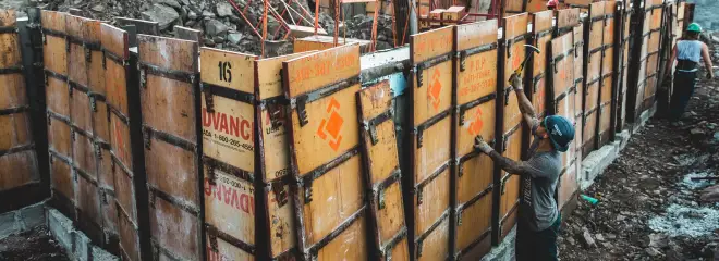 Ouvrier qui ajuste au marteau des panneaux de coffrage marqués « BATI-FORME 418-387-3300 », montés à même le roc.