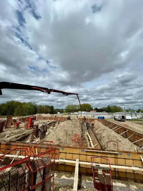 Chantier d’excavation où les panneaux de coffrage sont montés, une pompe à béton déployée au-dessus.