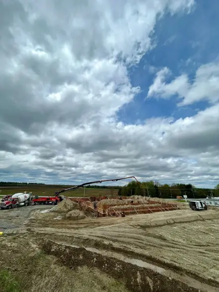 Solage coffré au fond d’une excavation, deux bétonnières et une pompe à béton rangées en bordure du chantier.