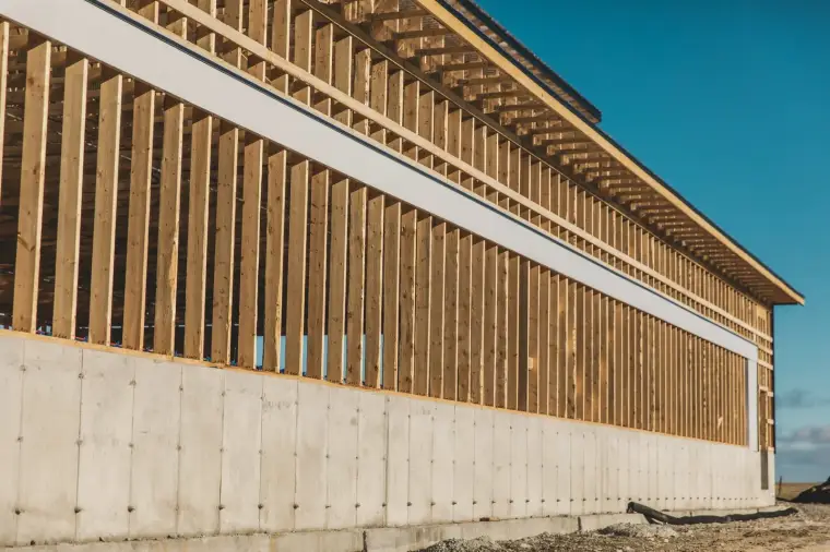 Mur de fondation de béton avec ses marques de tiges d’ancrage, surmonté d’une charpente de bois.